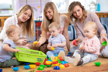 Obraz premium Group of children 1-2 years old playing in kindergarten or daycare centre under the supervision of moms