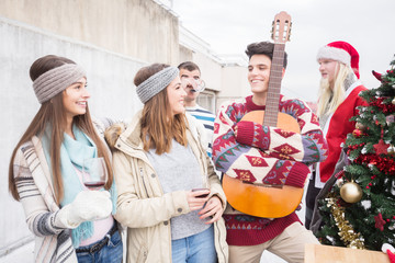 Young man smiling with friends and holding guitar on balcony on Christmas