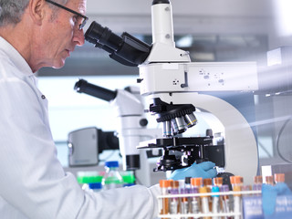 Side view of male scientist analyzing blood samples through microscope in laboratory