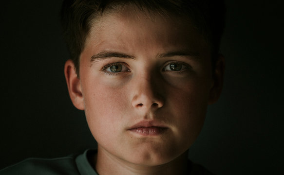 Close-up Portrait Of Serious Boy Standing In Darkroom At Home