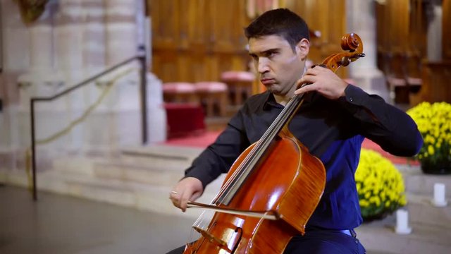 emotional male cellist is playing in church hall, performing dramatic classical music, moving bow over strings