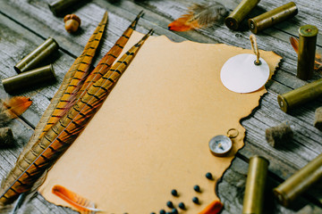Closeup feather and cartridges on vintage paper for information on old wooden background. Hunting...