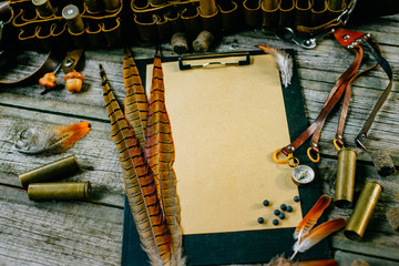 Pheasant feather and brass cartridge on clipboard with vintage paper for information on old wooden...