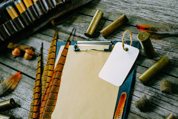 Closeup feather and cartridges on clipboard with vintage paper and square label for information on...