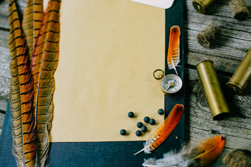 Closeup pheasant feather and cartridges on clipboard with vintage paper for information on old...