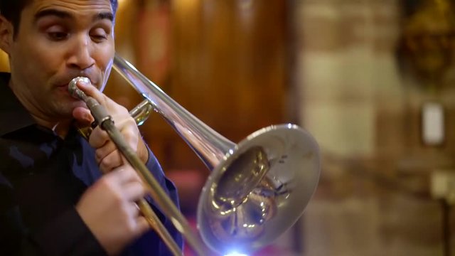 male trumpeter is playing in hall of church, performing jazz, close-up of his face, fingers, moving camera