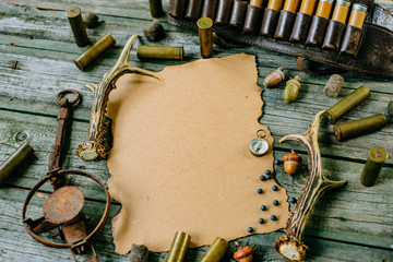 Closeup paper for information on old wooden background and deer horn, trap and cartridges beside. Hunting equipment on vintage board.