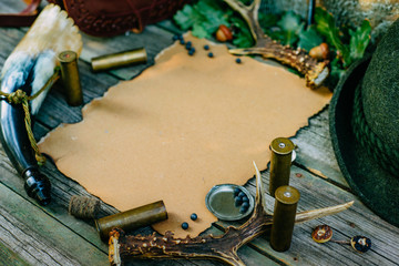 Closeup paper for information on old wooden background and deer horn, huntsman hat and cartridges beside. Hunting equipment on vintage board.