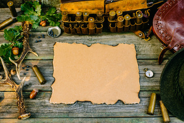Vintage paper in the center of hunting equipment, oak and horns around of old wood board. Top view