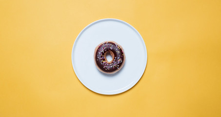 Overhead view of chocolate donut with sprinkles in plate on yellow background