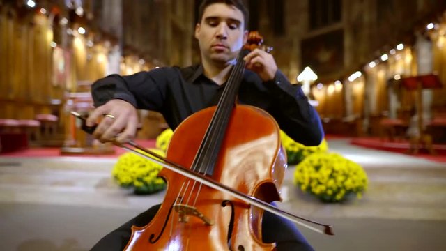 adult man is playing cello in christian church, performing composition on a concert for parishioners, classical music
