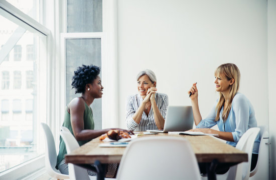 Happy businesswomen discussing at conference table in creative office