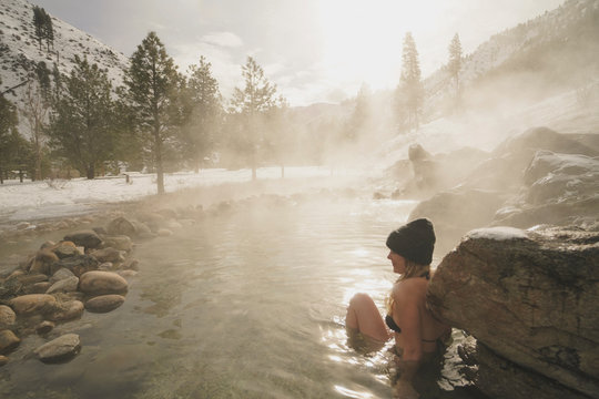 Woman wearing bikini sitting in thermal pool at forest during winter