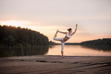 Woman practicing yoga on pier during sunset