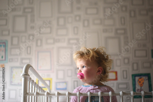 Toddler with pacifier standing in crib at home