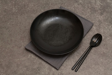 Black plate, Cutlery and napkin on grey stone table. Top view
