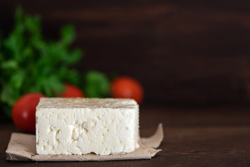 Large piece of feta cheese on dark wooden table. Selective focus