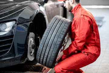 Car service worker in red uniform changing wheel of a sport car at the tire mounting service