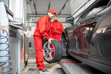 Two car service workers in red uniform changing wheel of a sport car at the tire mounting service