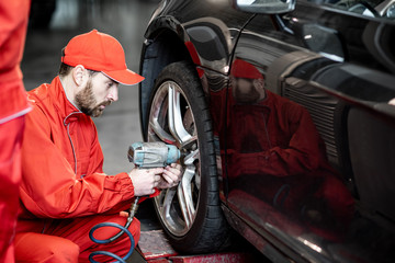 Car service worker in red uniform changing wheel of a sport car at the tire mounting service