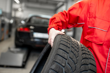 Fototapeta premium Worker in uniform carrying new tires at the car service or store, close-up view