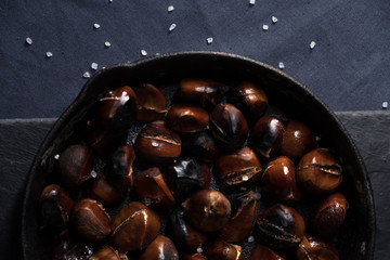 Fried chestnuts with sea salt in rustic pan served on blue table cloth