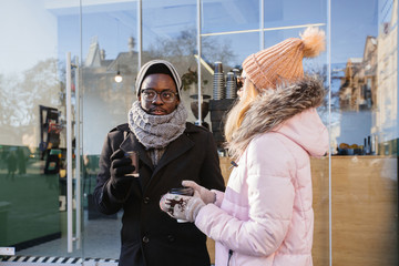 Mixed race positive smiling couple drinking coffee walking outdoor over modern cafe shop window in...