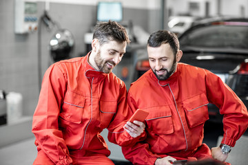 Car service workers in red uniform having a break sitting together with phone on the wheels at the tire mounting service