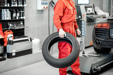 Car service worker in red uniform carrying new tires at the tire mounting service or shop