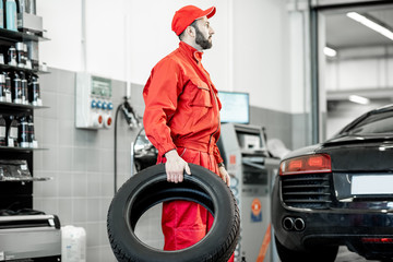 Car service worker in red uniform carrying new tires at the tire mounting service or shop