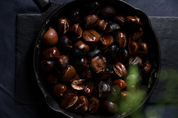 Fried chestnuts served on blue table cloth under Christmas decorated thuja