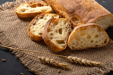 Italian traditional ciabatta bread with sliced ​​pieces and ears of wheat lie on a jute napkin...