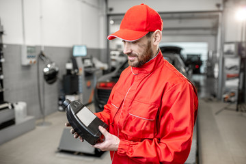 Portrait of a handsome auto mechanic in red uniform holding bottle with engine oil at the car service