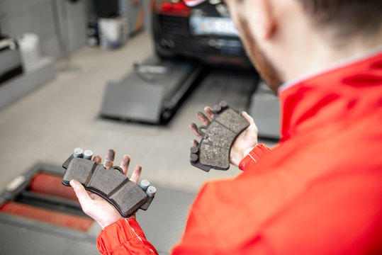Auto mechanic holding new and used brake pads at the car service, close-up view