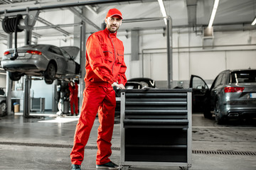 Two auto mechanics in red uniform walking with working cart at the car service