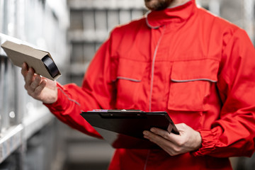 Warehouse worker in red uniform filling some documents checking goods at the storage