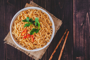 Cooked instant noodles in bowl with chopsticks in top view closeup on wooden table with copy space