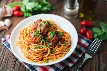 Spaghetti and meatballs with tomato sauce in white dish on wooden rustic board, Italian food closeup and top view.