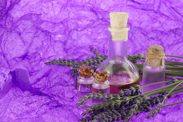 Lavender oil set and fresh lavender flowers on a bright purple background of crumpled paper