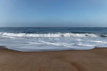 Fototapeta na wymiar Foamy Atlantic ocean wave on Nazare city beach, Portugal.