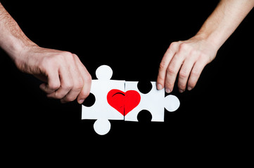 Puzzle with a red heart in the hands of a loving couple. Valentine's day concept.On a black background