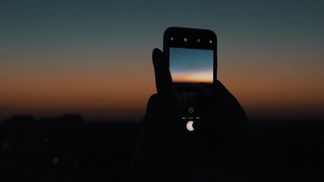 girl makes a photo of the city on a smartphone at sunset.