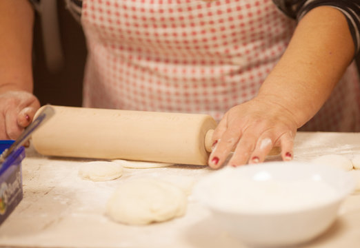 Female hands rolling out dough on kitchen table, close up 