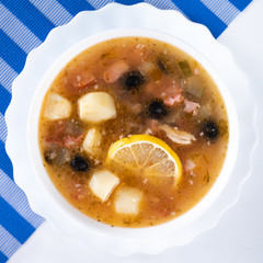 Traditional Russian soup Solyanka cooked with meat, sausages, salted cucumbers on wite bowl. Black...