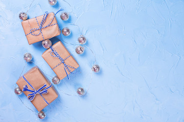 Fototapeta na wymiar Wrapped boxes with presents and silver fairy lights on blue textured background. Top view.