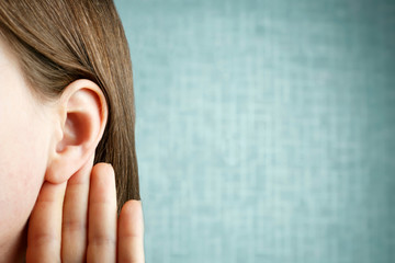 The girl listens attentively with her palm to her ear, close-up, indoors, the news concept