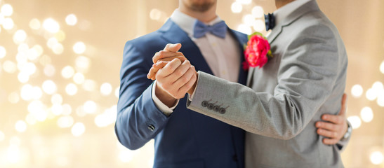 lgbt, homosexuality and same-sex marriage concept - close up of happy male gay couple holding hands and dancing on wedding over festive lights background