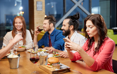 Fototapeta na wymiar technology, lifestyle and people concept - bored woman dining with friends and messaging on smartphone at restaurant