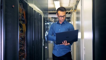 A man with a laptop standing in a server room