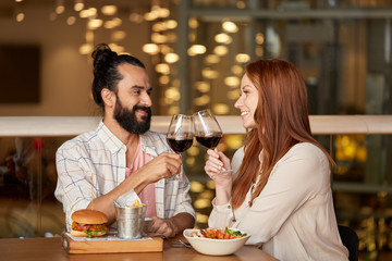 celebration, leisure and holidays concept - happy young couple eating and clinking glasses of red wine at restaurant